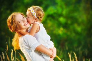 Happy family on a summer meadow. little girl child baby daughter hugging and kissing mother